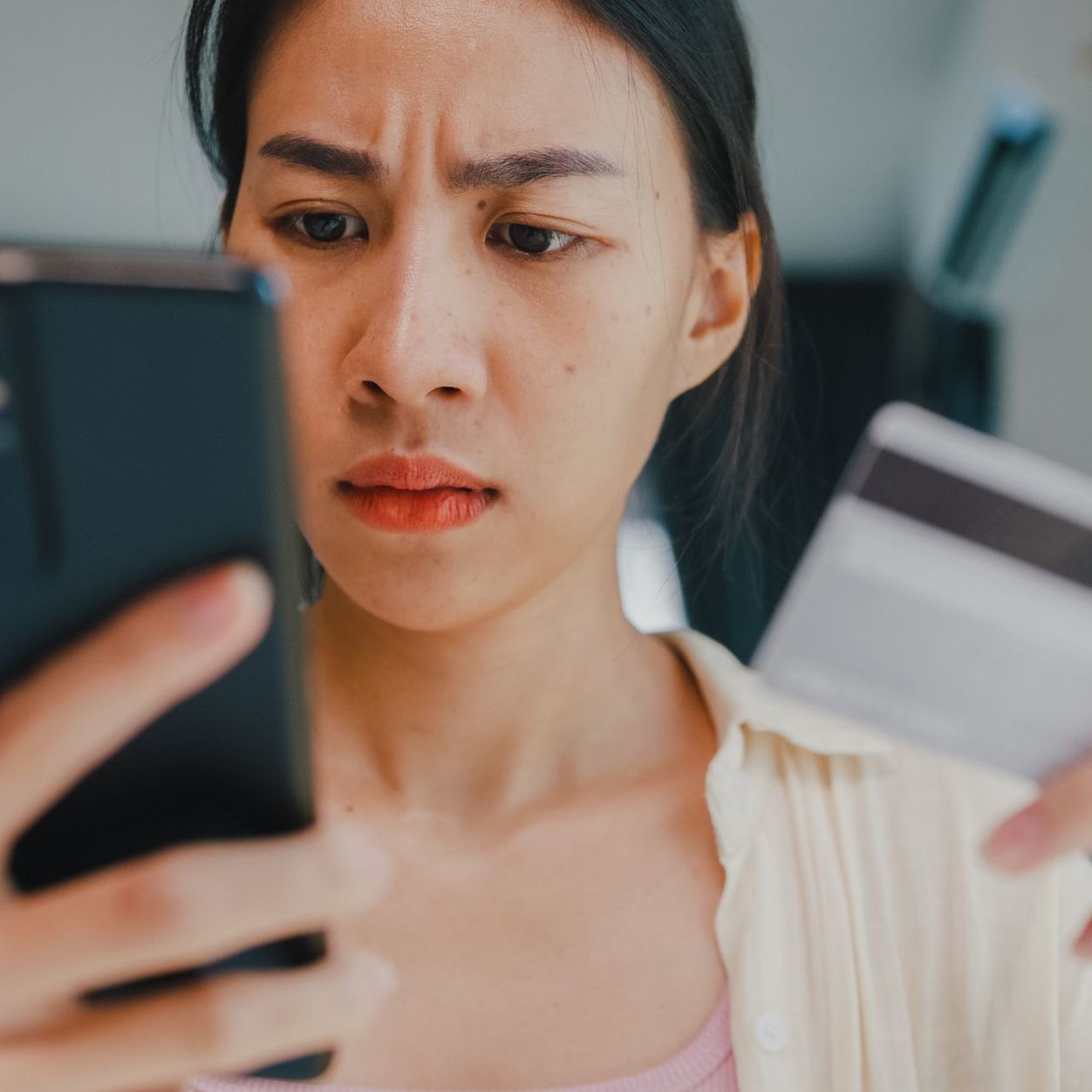 Close-up Youth asia female wear casual sit front of desk hold smartphone and credit card feel upset online shopping payment declined credit over limit in living room at house.